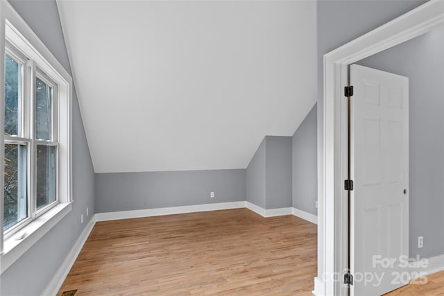 additional living space with baseboards, vaulted ceiling, and light wood-type flooring