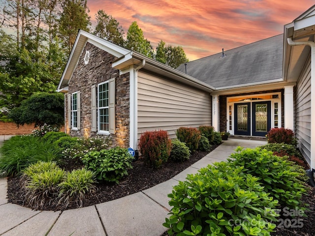 exterior entry at dusk featuring french doors and stone siding
