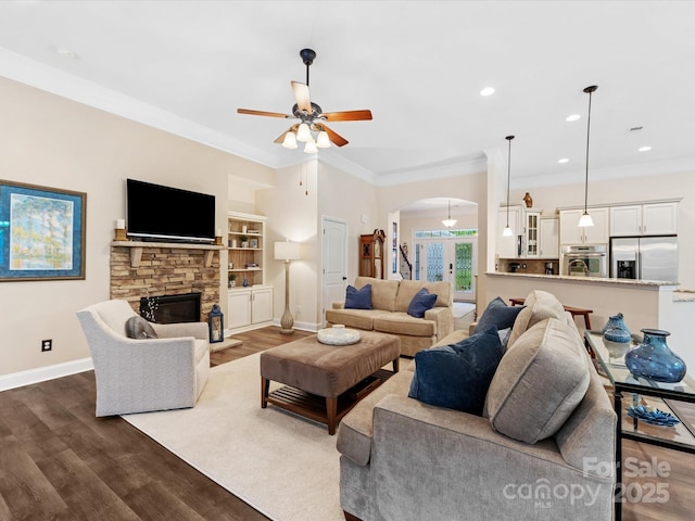 living room featuring a ceiling fan, baseboards, dark wood-style flooring, crown molding, and arched walkways