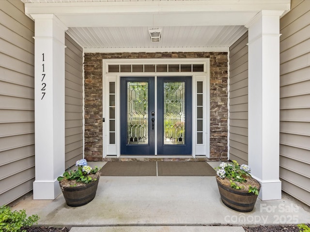 view of exterior entry featuring stone siding, a porch, and french doors