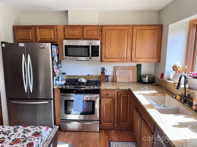 5A Hedgerose Ct, Asheville, NC 28805 - kitchen with wood finished floors, brown cabinets, light stone counters, a sink, and appliances with stainless steel finishes