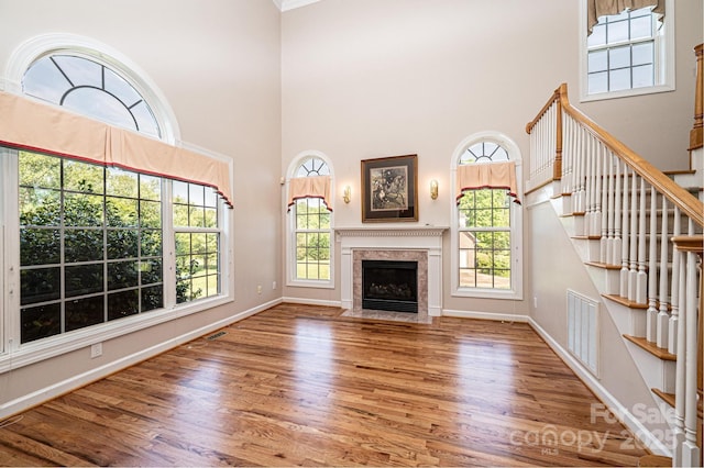 unfurnished living room with visible vents, a towering ceiling, wood finished floors, and a healthy amount of sunlight