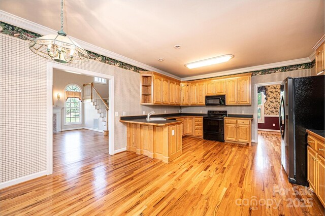 kitchen featuring an inviting chandelier, a peninsula, wallpapered walls, ornamental molding, and black appliances