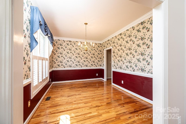 unfurnished dining area featuring crown molding, a notable chandelier, wood finished floors, and a healthy amount of sunlight