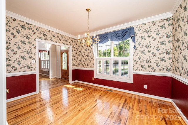 unfurnished dining area featuring crown molding, wallpapered walls, wood finished floors, and a notable chandelier