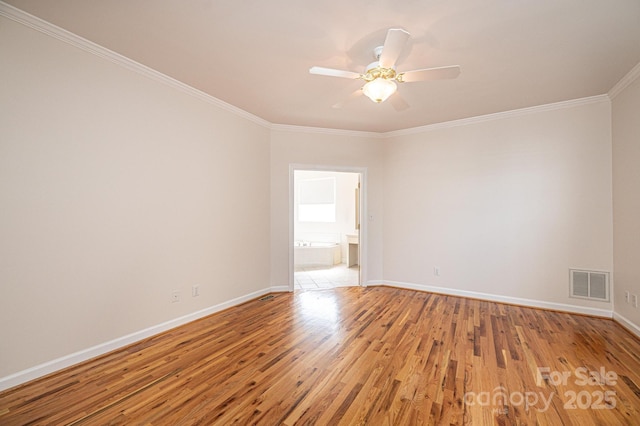 empty room with crown molding, light wood finished floors, a ceiling fan, baseboards, and visible vents
