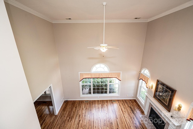 unfurnished living room featuring visible vents, ornamental molding, wood finished floors, baseboards, and a high ceiling
