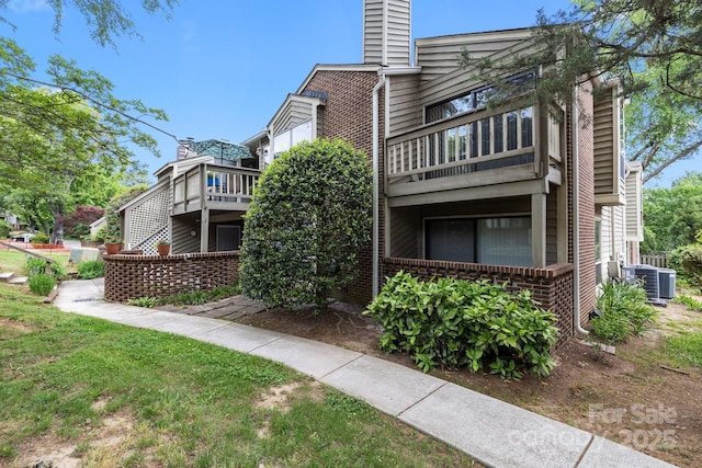 view of side of home with brick siding, central AC, a chimney, and a balcony