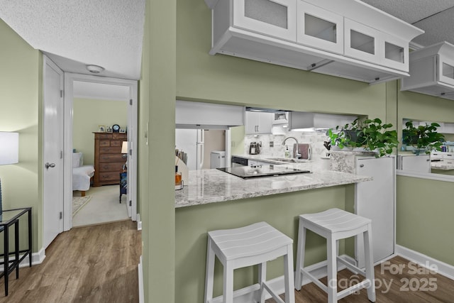 kitchen featuring white cabinetry, wood finished floors, tasteful backsplash, and glass insert cabinets