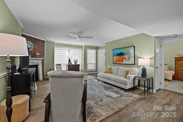 living area featuring crown molding, wood finished floors, a fireplace, ceiling fan, and a textured ceiling