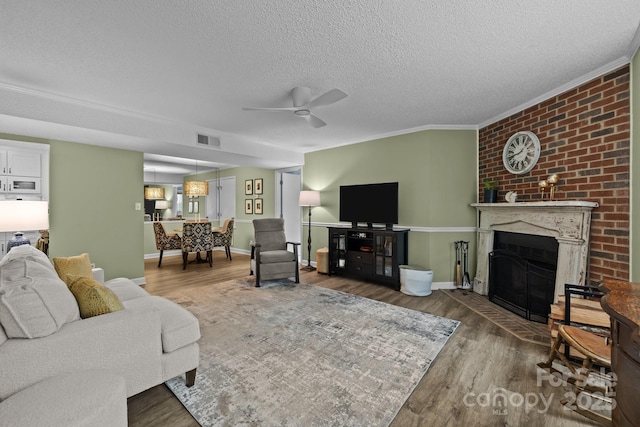 living area with a ceiling fan, a textured ceiling, visible vents, crown molding, and wood finished floors