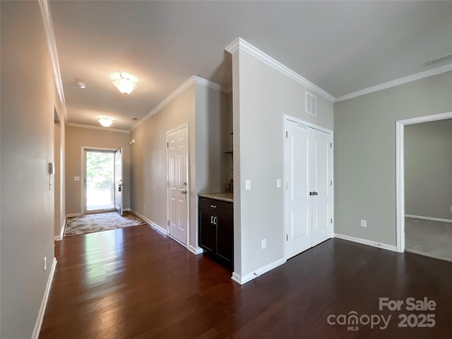 corridor featuring visible vents, ornamental molding, dark wood finished floors, and baseboards