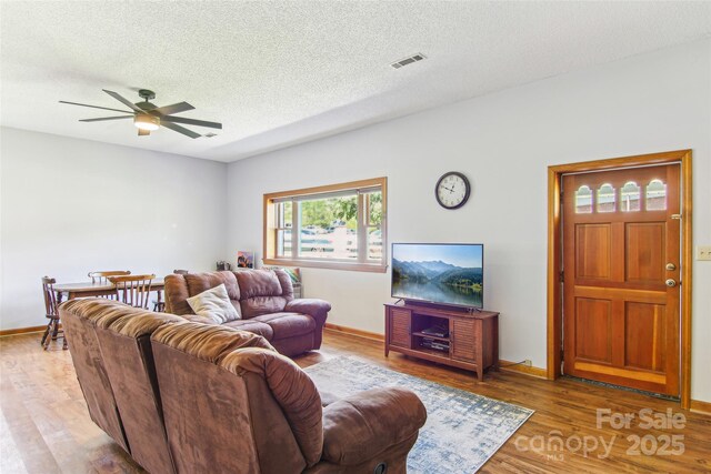 living area featuring visible vents, wood finished floors, baseboards, ceiling fan, and a textured ceiling