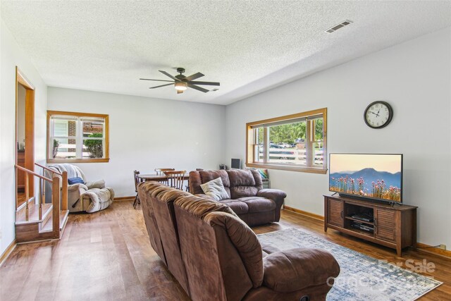 living area featuring ceiling fan, a textured ceiling, visible vents, wood finished floors, and baseboards