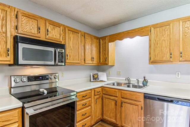 kitchen featuring a textured ceiling, appliances with stainless steel finishes, brown cabinets, a sink, and light countertops
