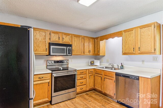 kitchen featuring a sink, light wood finished floors, appliances with stainless steel finishes, and light countertops