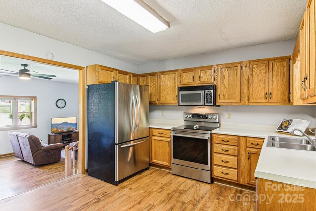 kitchen featuring light wood-type flooring, light countertops, a textured ceiling, a sink, and stainless steel appliances