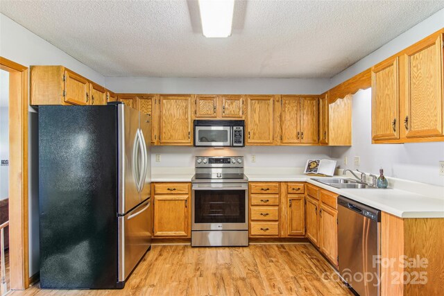 kitchen with light countertops, a textured ceiling, a sink, light wood finished floors, and stainless steel appliances