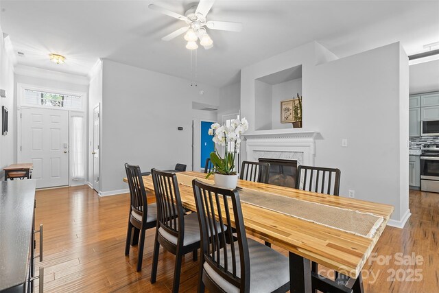 dining room with ceiling fan, wood finished floors, baseboards, ornamental molding, and a premium fireplace