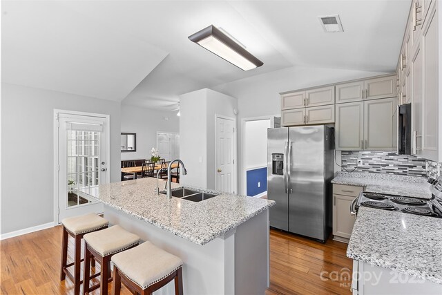 kitchen featuring appliances with stainless steel finishes, a sink, wood finished floors, lofted ceiling, and visible vents
