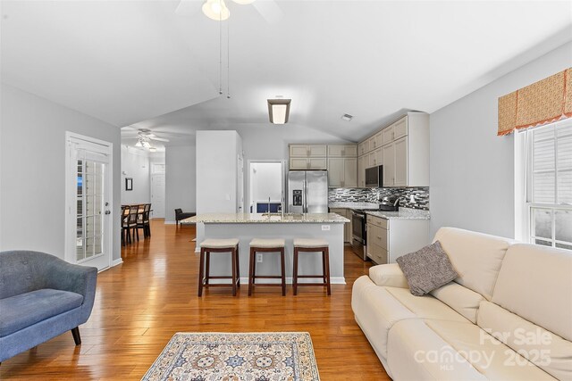 living area featuring visible vents, ceiling fan, wood finished floors, and vaulted ceiling