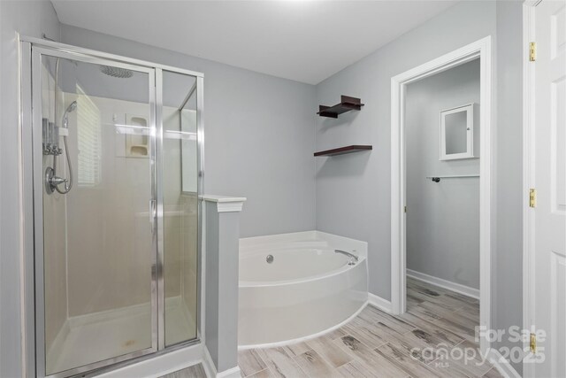 full bath featuring baseboards, a stall shower, a bath, and wood finished floors