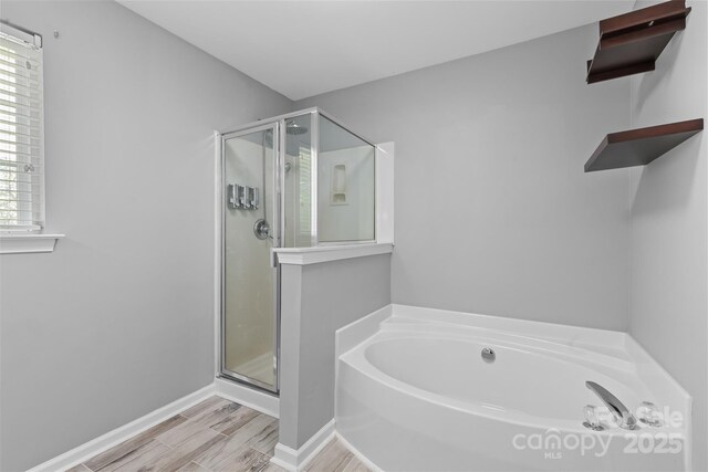 bathroom with wood finished floors, a bath, baseboards, and a stall shower
