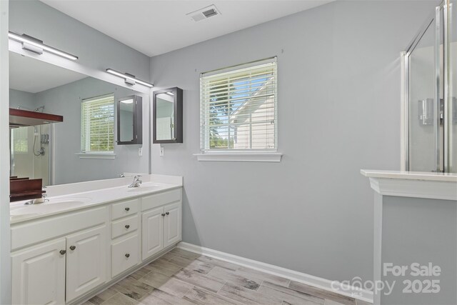 bathroom featuring visible vents, double vanity, wood finished floors, a sink, and a stall shower