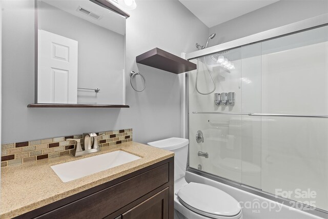 bathroom with vanity, toilet, decorative backsplash, combined bath / shower with glass door, and visible vents
