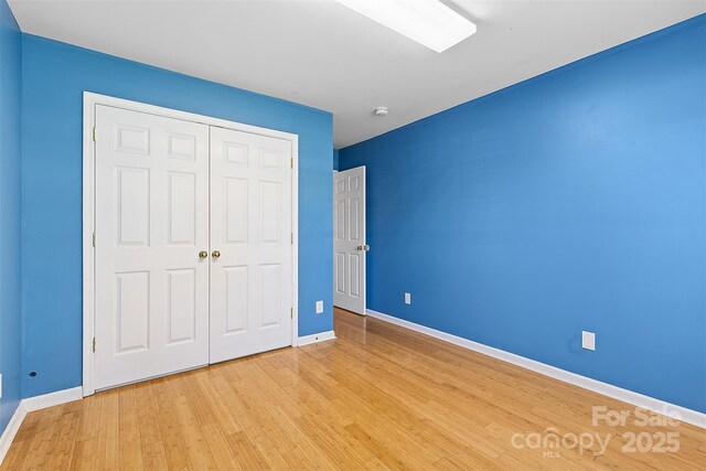 unfurnished bedroom with baseboards, light wood finished floors, and a closet