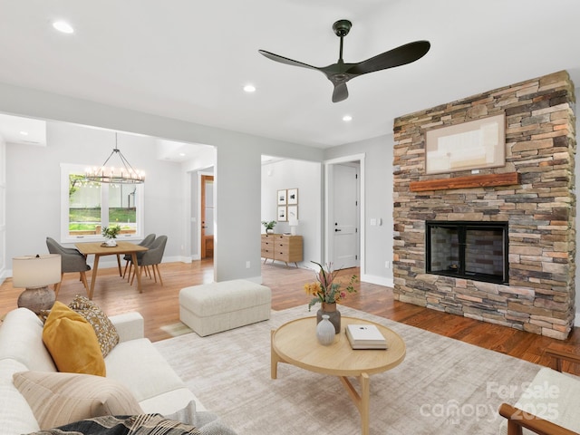 living room featuring baseboards, a stone fireplace, ceiling fan with notable chandelier, and wood finished floors