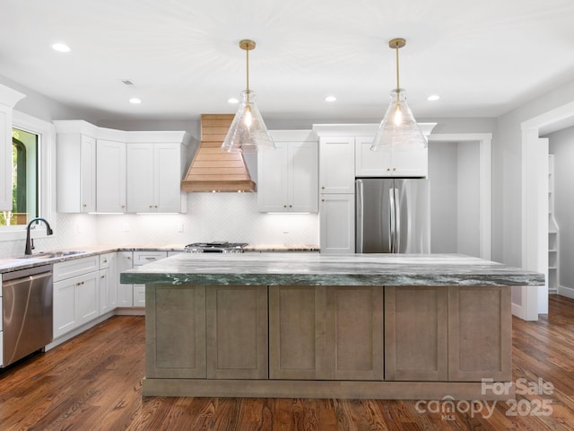 kitchen with a sink, custom exhaust hood, white cabinetry, and appliances with stainless steel finishes
