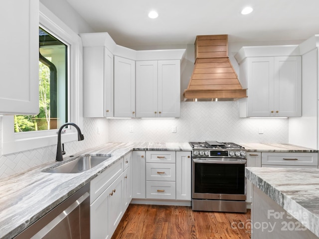 kitchen with a sink, custom exhaust hood, stainless steel appliances, and white cabinets