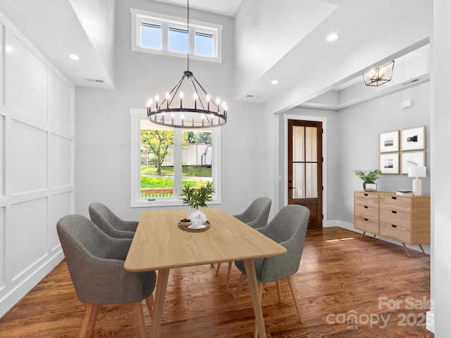 dining area with wood finished floors, a notable chandelier, baseboards, a towering ceiling, and recessed lighting