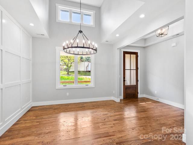 unfurnished dining area with baseboards, recessed lighting, wood finished floors, and a chandelier