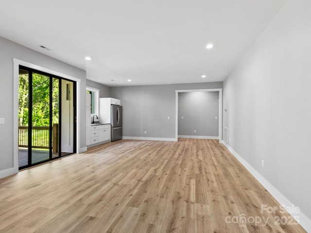 unfurnished living room featuring a sink, visible vents, recessed lighting, light wood-style flooring, and baseboards