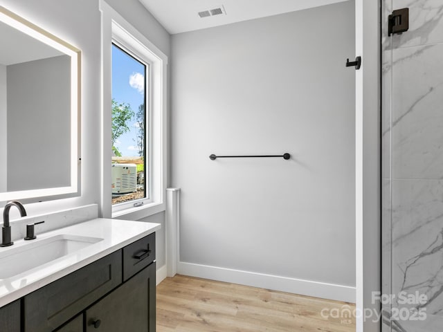 bathroom featuring baseboards, visible vents, vanity, wood finished floors, and a marble finish shower