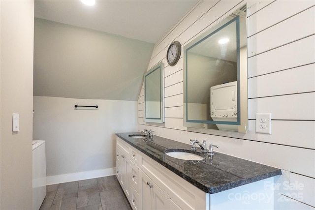 bathroom with baseboards, double vanity, and stacked washing machine and dryer