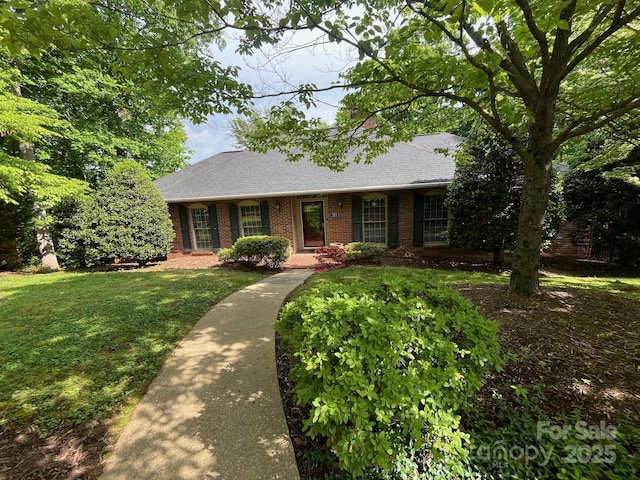 ranch-style home with brick siding, roof with shingles, and a front yard