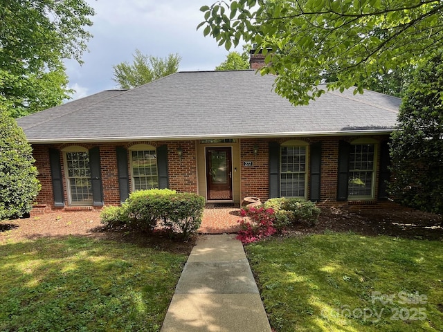 ranch-style house with a porch, a chimney, a front yard, roof with shingles, and brick siding