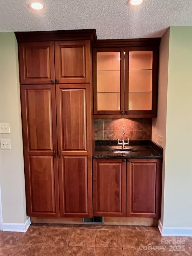 bar with a textured ceiling, baseboards, visible vents, and a sink