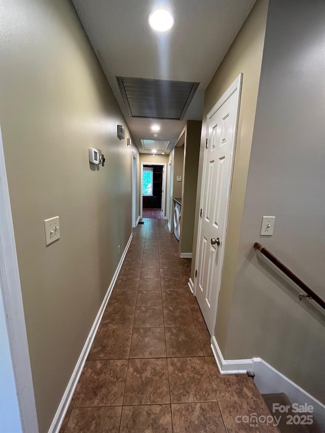 hallway with dark tile patterned floors, baseboards, an upstairs landing, and attic access