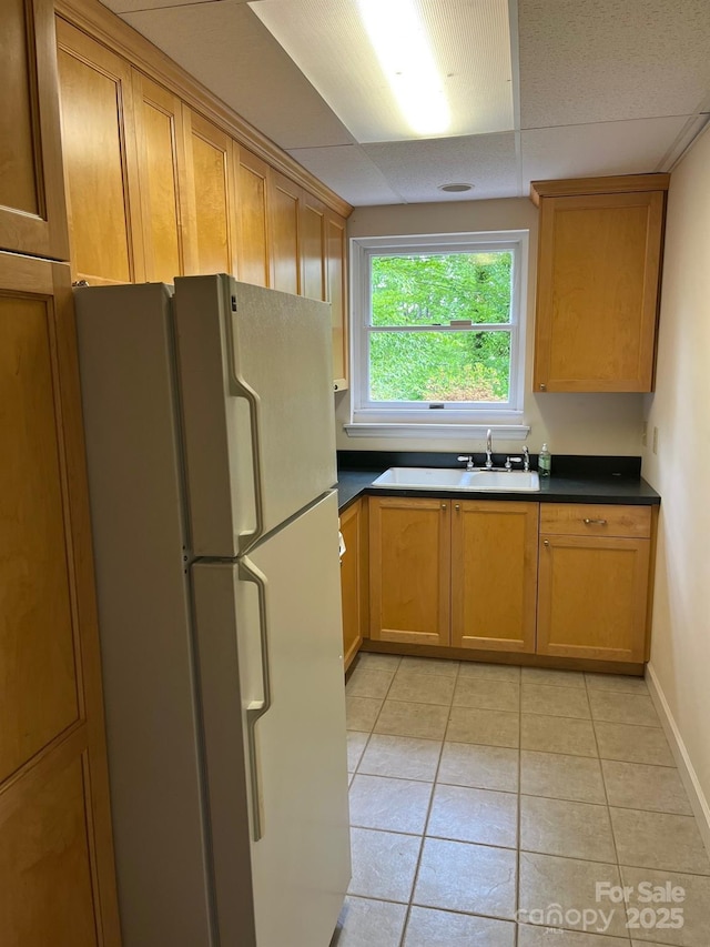 kitchen featuring freestanding refrigerator, dark countertops, a sink, and light tile patterned floors