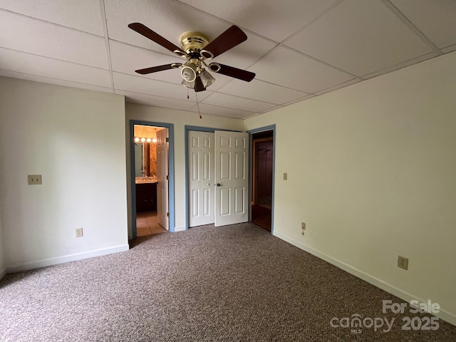 unfurnished bedroom with carpet, a ceiling fan, baseboards, a drop ceiling, and ensuite bathroom