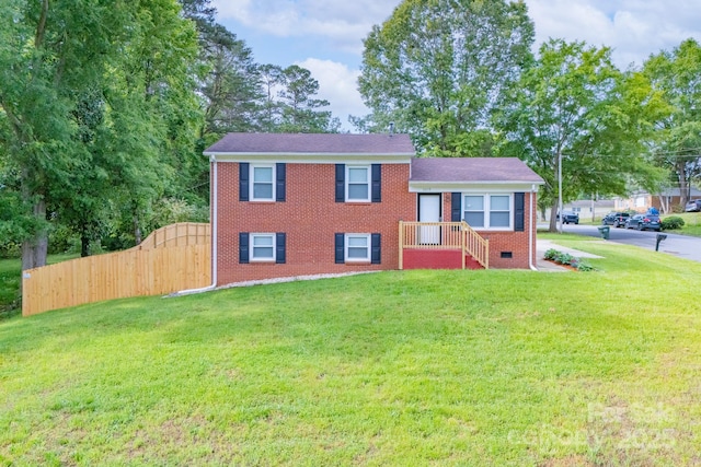tri-level home featuring fence, a gate, a front lawn, and brick siding
