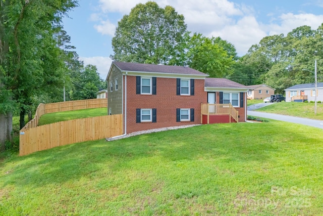tri-level home with brick siding, fence, and a front lawn