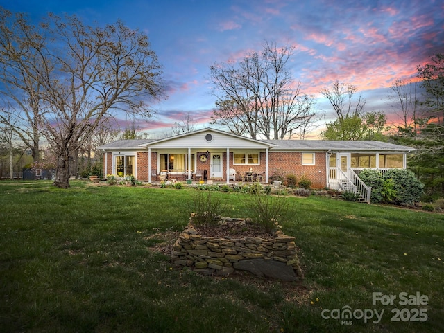 view of front of property featuring a porch, a yard, and brick siding