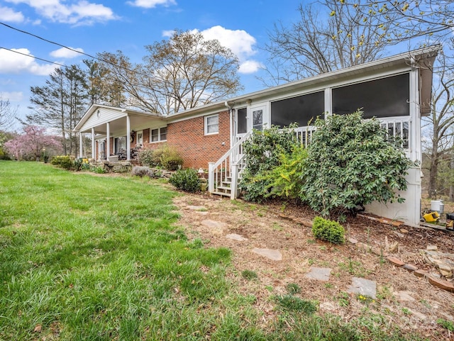exterior space with a yard, covered porch, a sunroom, and brick siding