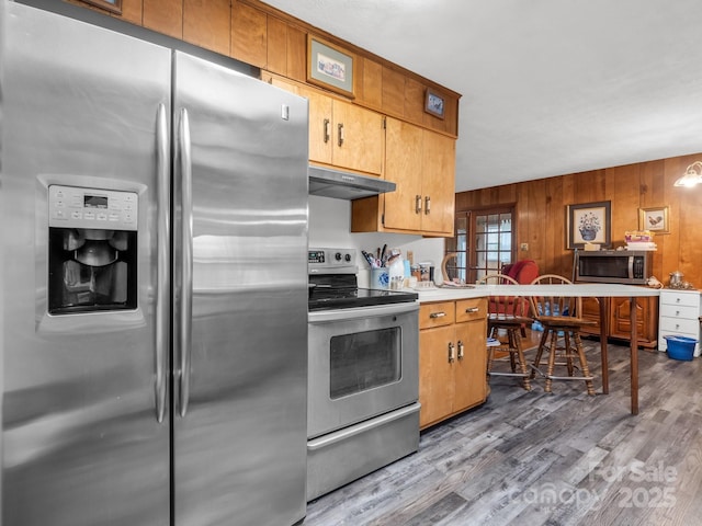kitchen featuring light wood-type flooring, light countertops, under cabinet range hood, wooden walls, and stainless steel appliances