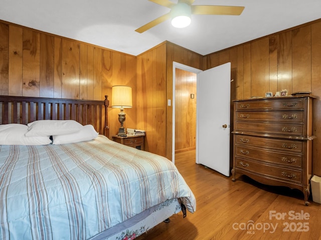 bedroom featuring wooden walls, a ceiling fan, and light wood-style flooring